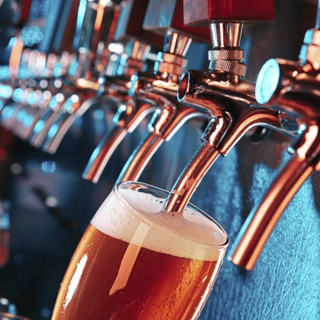 Cerveza dorada siendo vertida en un vaso transparente, creando espuma en la parte superior.